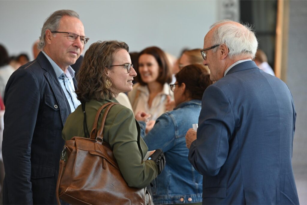 Group of professionals conversing at a networking event; woman with curly hair and glasses in the foreground.